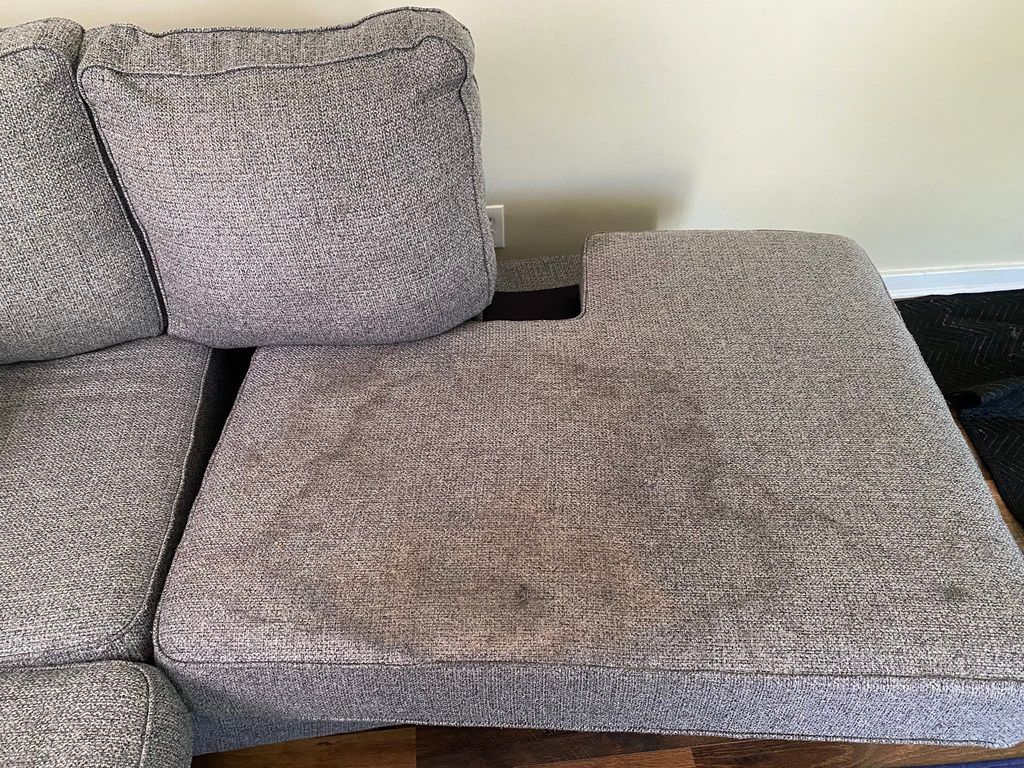 A grey sectional cushion with dark soiling across the seat
