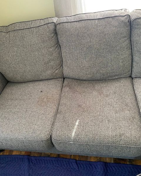 A grey sofa with dark stains on the seat cushions
